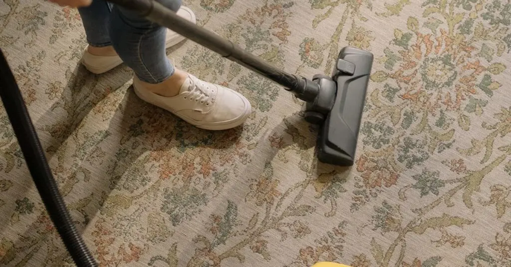 Person cleaning a floral carpet with a yellow vacuum cleaner indoors.